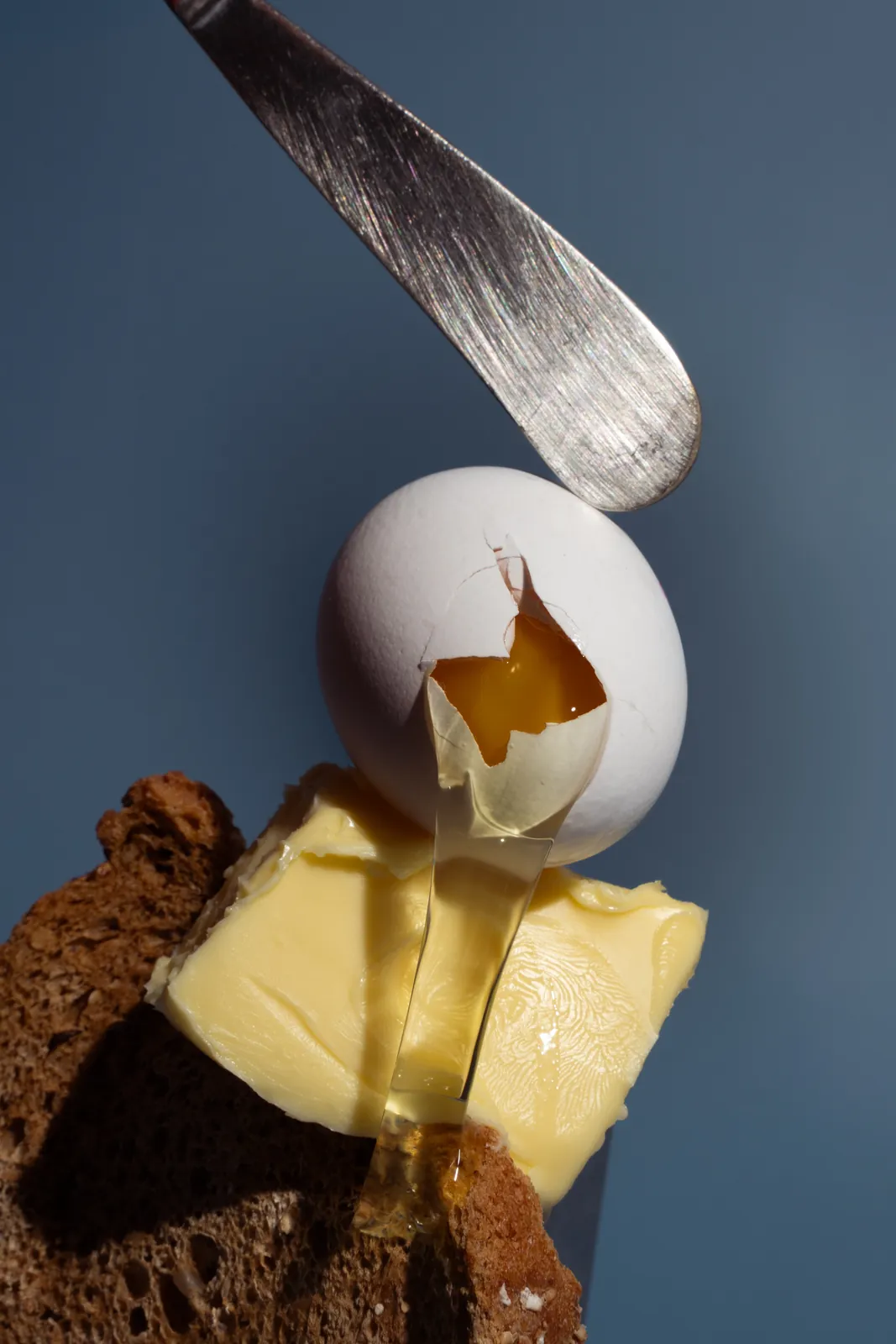 A knife hovering over an egg, butter, and dark bread