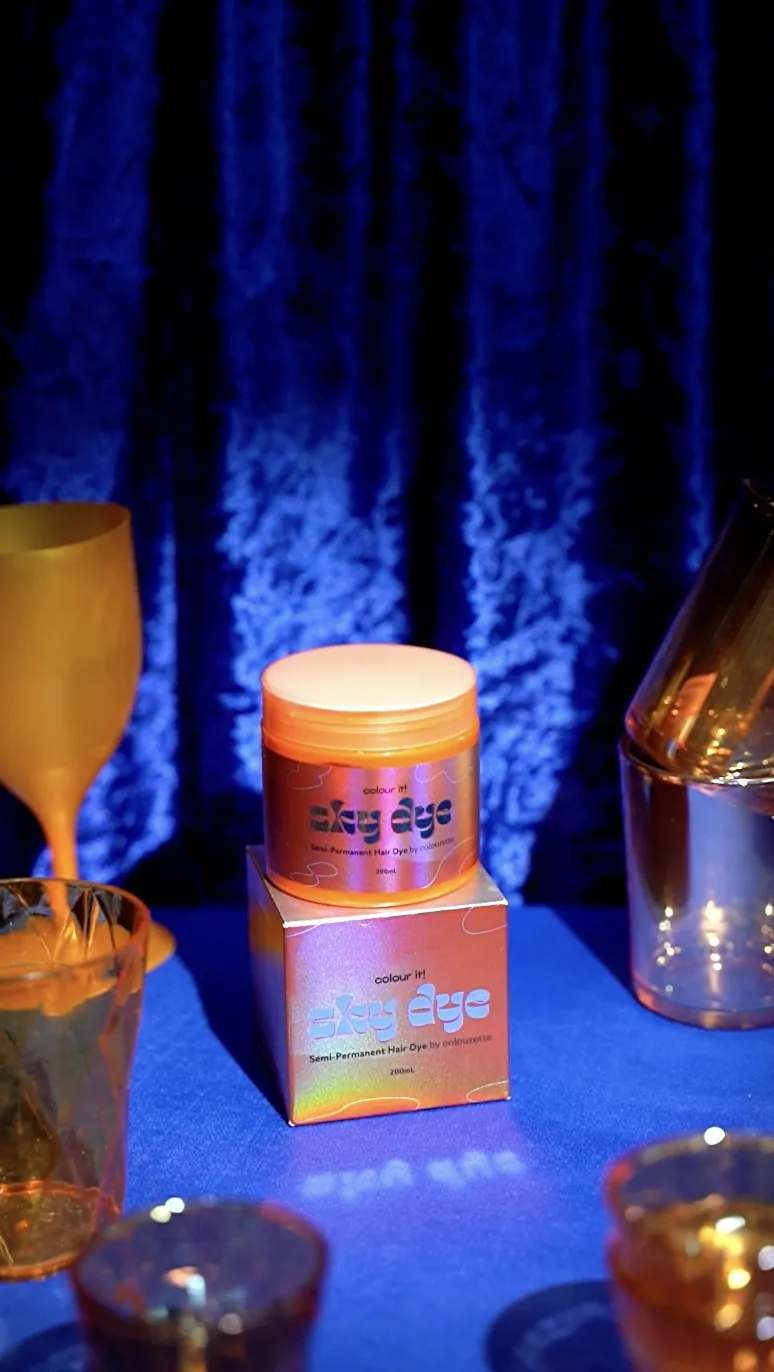 An orange jar glowing on blue crushed velvet among coloured glasses