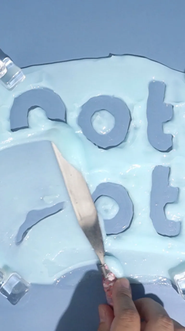 A palette knife lifting icy blue cream around the Not Pot logo